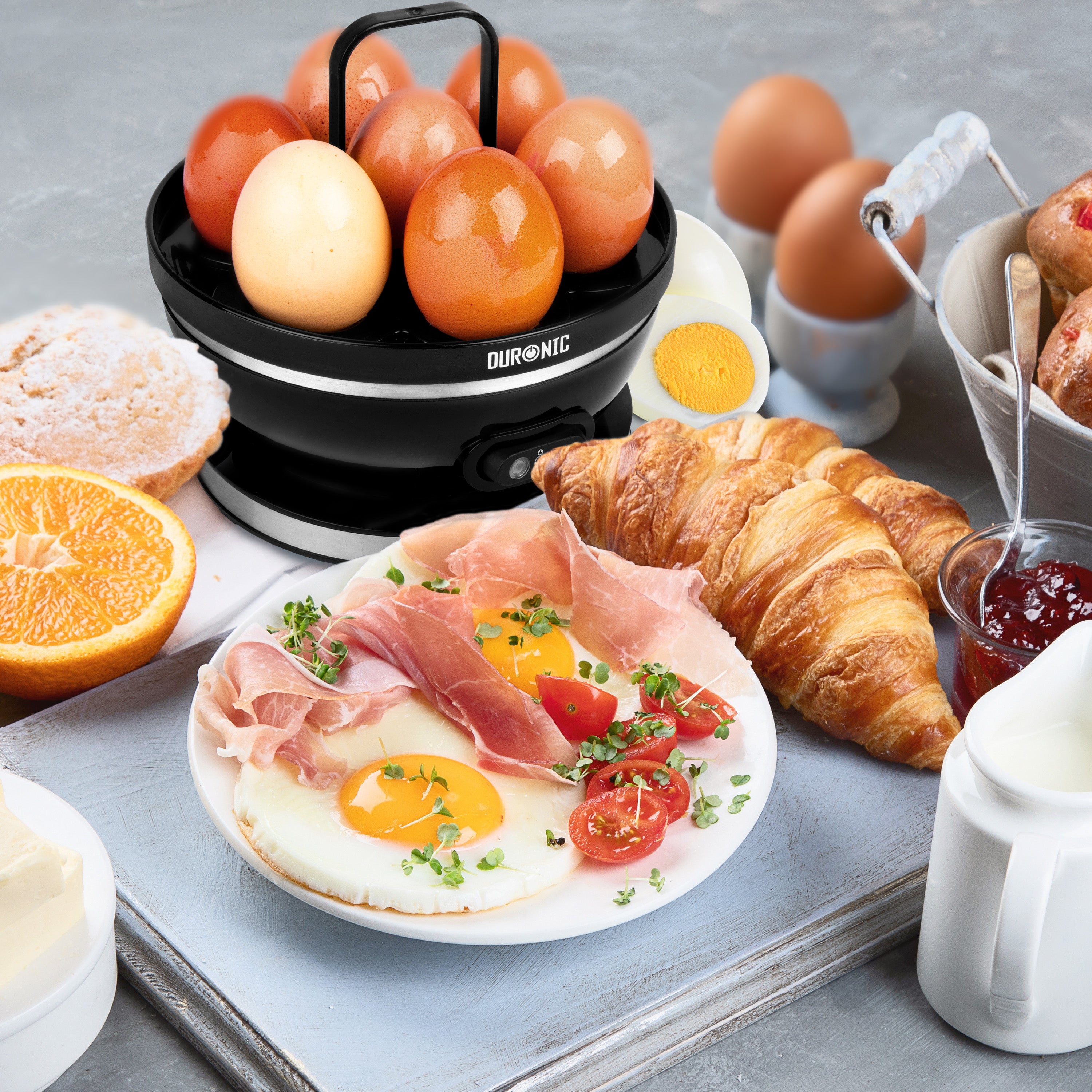Duronic EB27 BK electric egg boiler cooking 7 eggs surrounded by delicious food like croissanta