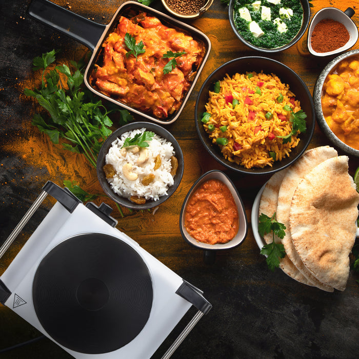 Duronic Electric Hot Plate HP1 WE sitting beside an assortment of colorful Indian food dishes.