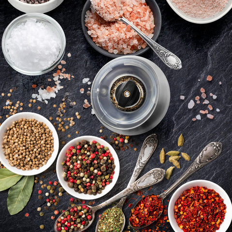 Duronic Electric Salt and Pepper Grinder with top view of colorful spices, gourmet salts, pepper grinder, and vintage spoons on dark slate.