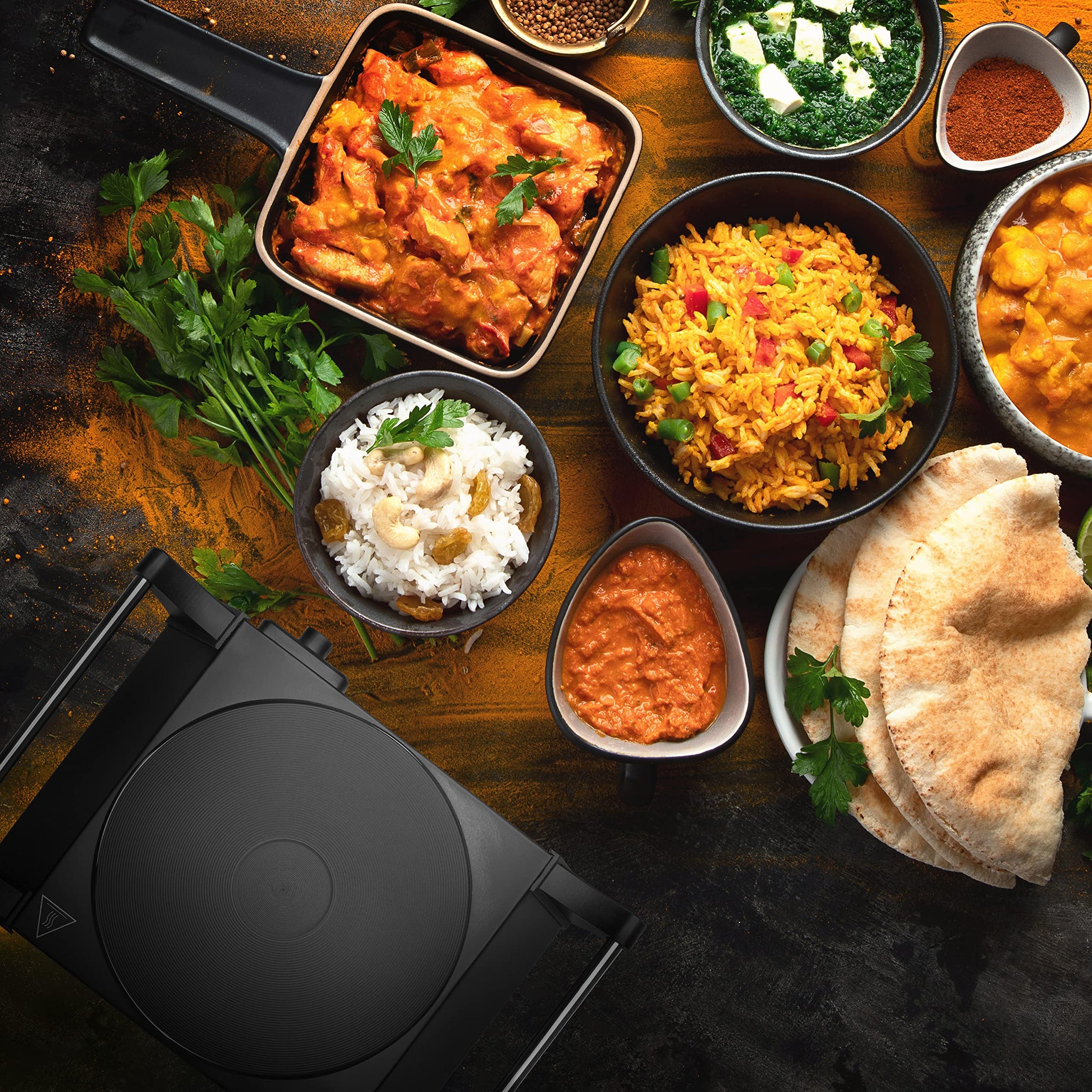 Duronic HP1 BK electric hot plate aesthetically shown in top-down view surrounded by dishes like rice, butter chicken, naan