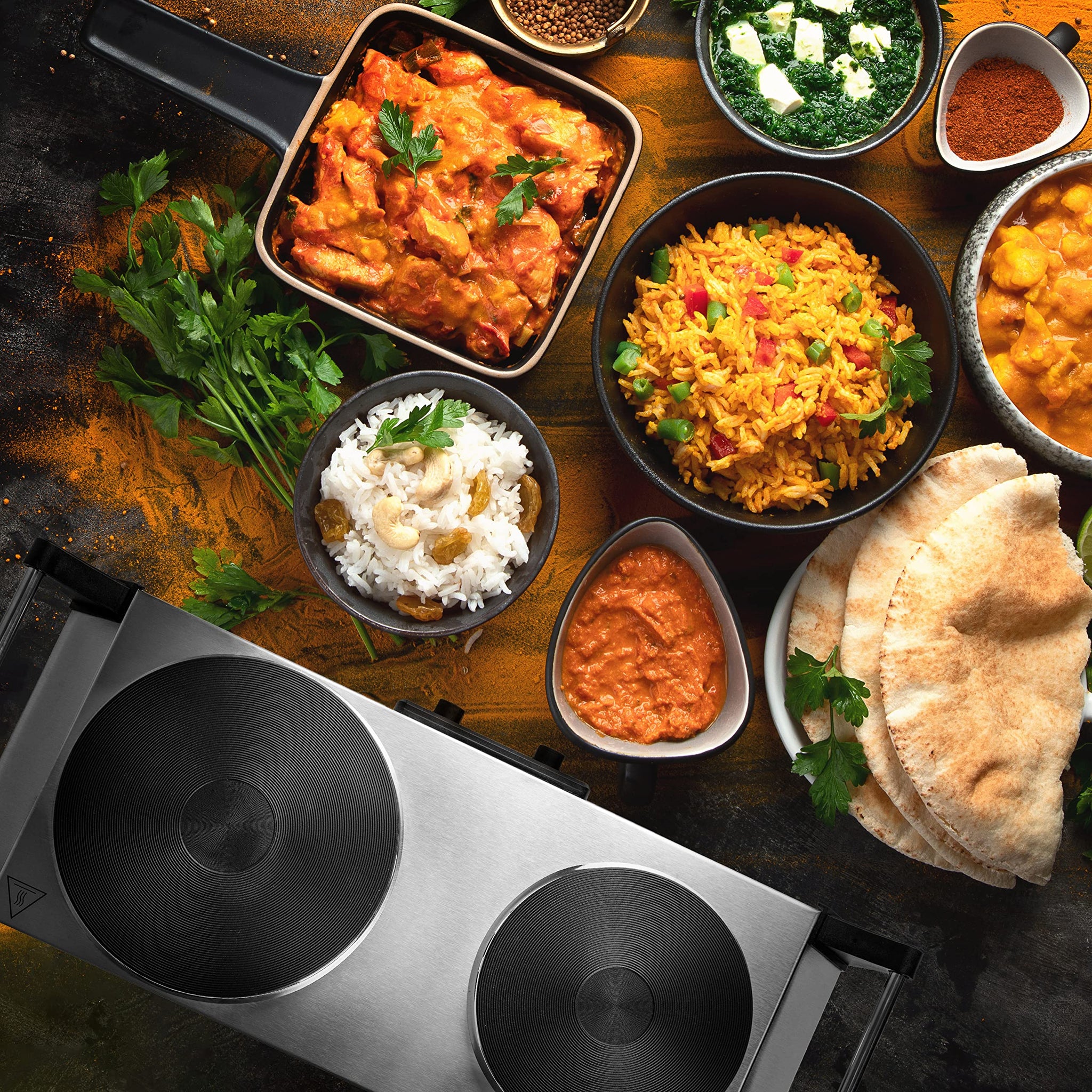 Duronic HP2 SS portable double hot plate surrounded by aesthetically pleasing dishes like butter chicken, naan, rice, biryani