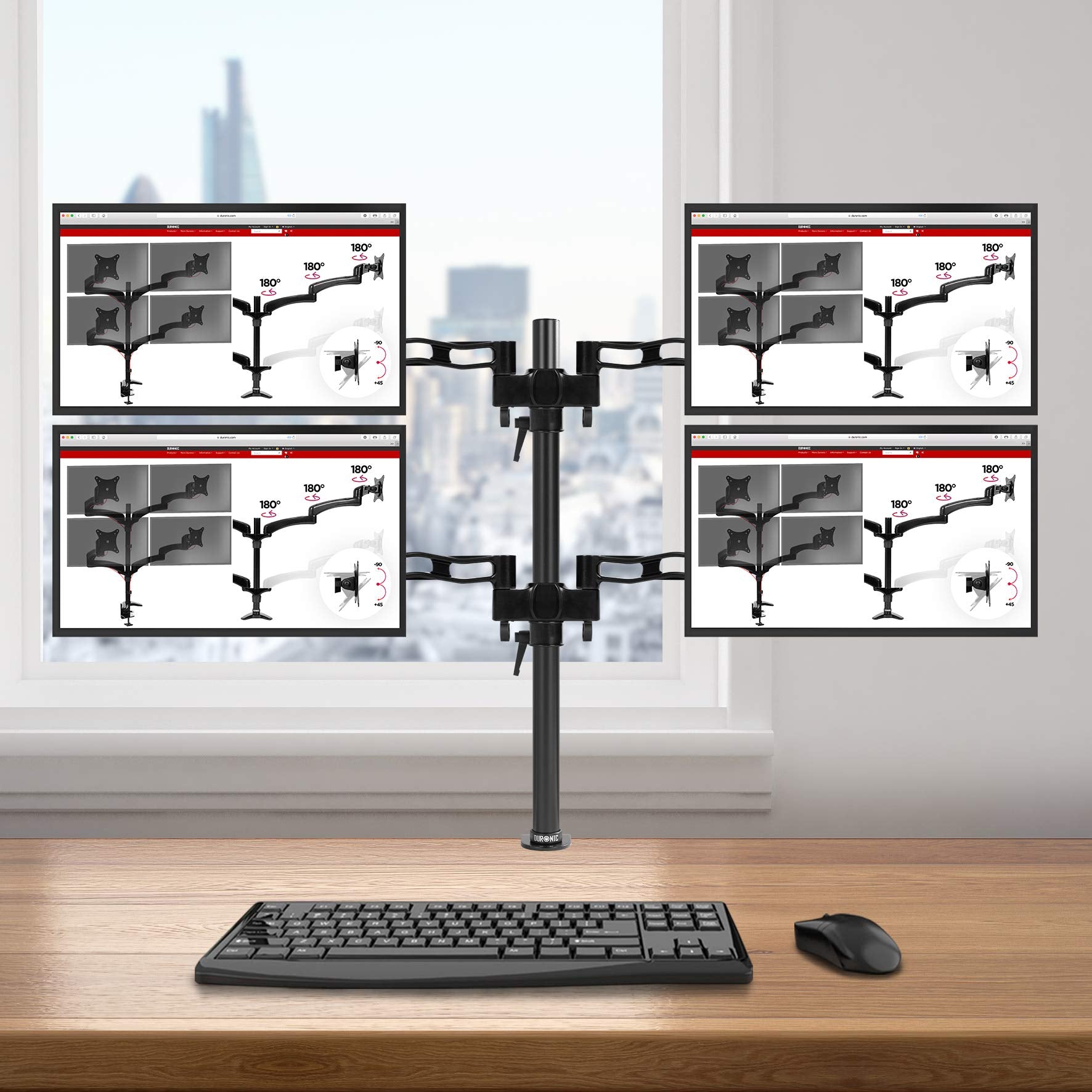 Duronic Quad Monitor Arm Stand holding four screens in a 2x2 grid over a wooden desk.