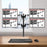 Duronic Quad Monitor Arm Stand holding four screens in a 2x2 grid over a wooden desk.