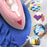 Duronic Travel Iron light smoothing out blue fabric, surrounded by circular icons showcasing its versatility for quilting, melty bead crafts, iron-on transfers, and travel.