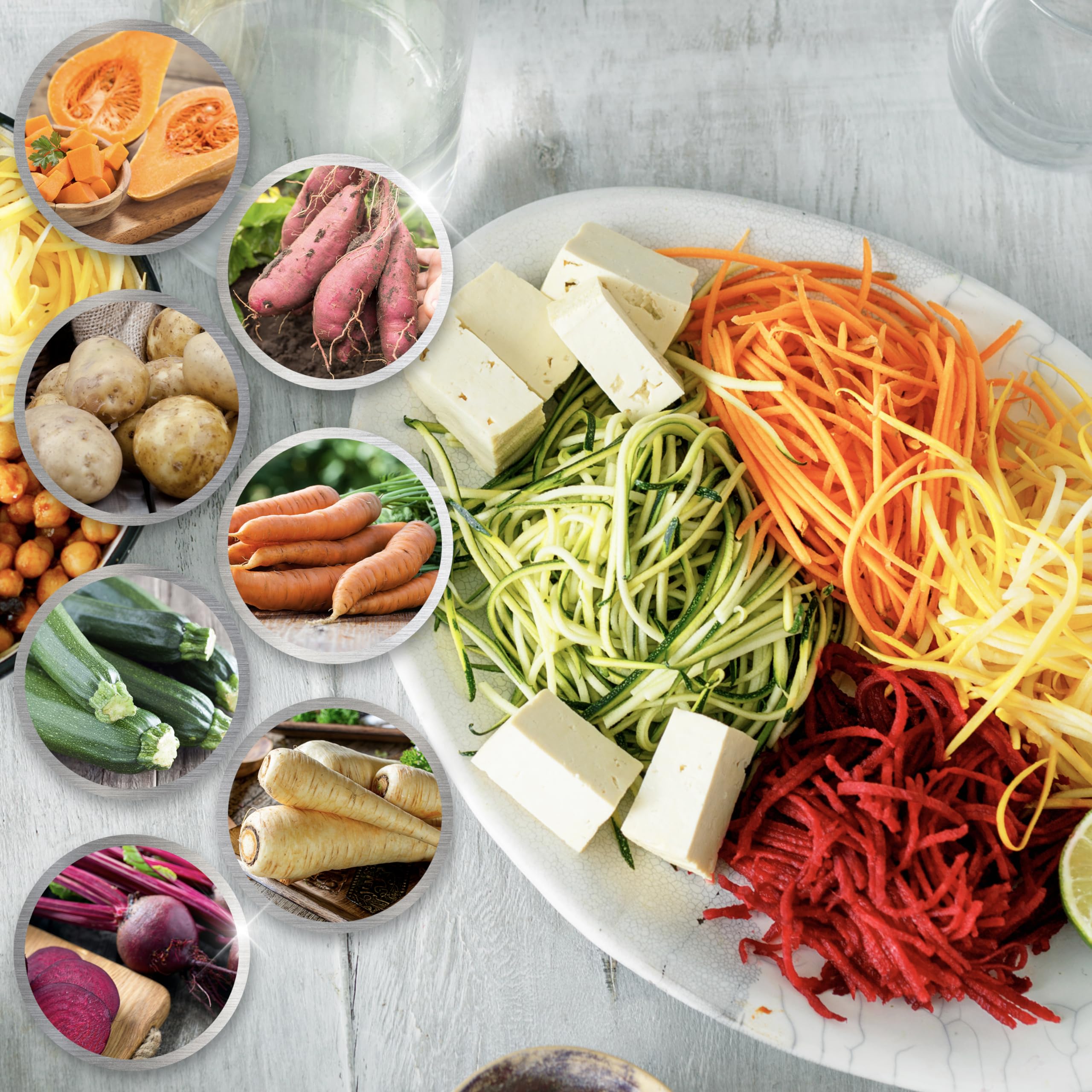 A vibrant assortment of spiralized vegetable noodles including zucchini, carrot, and beet served on a white platter with cubed tofu and circular insets showcasing the fresh whole vegetables.