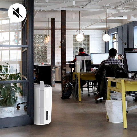 Duronic Dehumidifier stands in a modern, industrial-style open office where employees are working at desks.