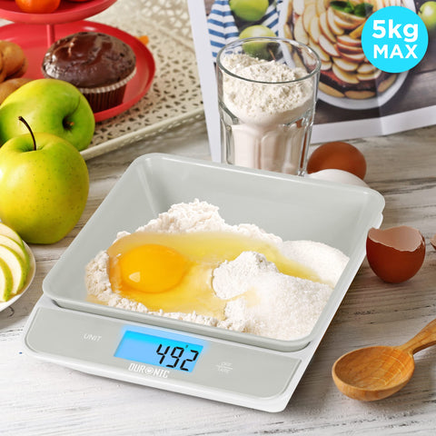 Duronic Digital Kitchen Scales weighing flour and an egg on a white counter with baking ingredients.