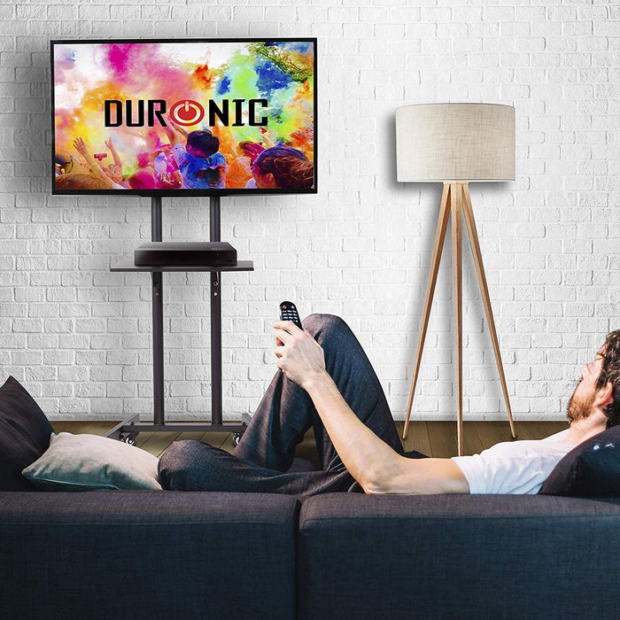 Duronic Mobile TV Stand on Wheels with a man on a sofa holding a remote control, watching a Duronic television on a rolling stand.
