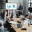 Duronic Mobile TV Stand on Wheels with a man presenting data charts on a large screen to colleagues in a modern office meeting.