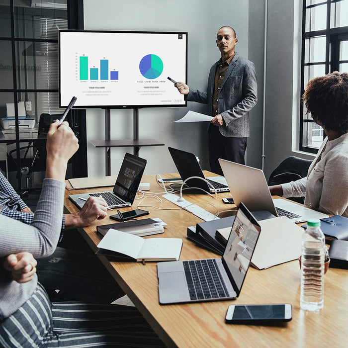 Duronic Mobile TV Stand on Wheels with a man presenting data charts on a large screen to colleagues in a modern office meeting.