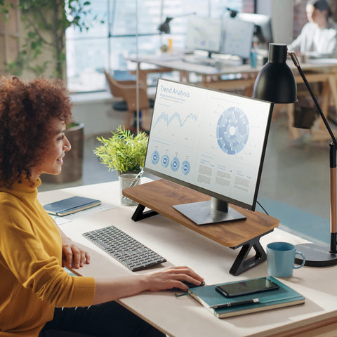 Duronic Monitor Stand Riser with woman in yellow sweater using a computer monitor on a wooden riser in a modern office.