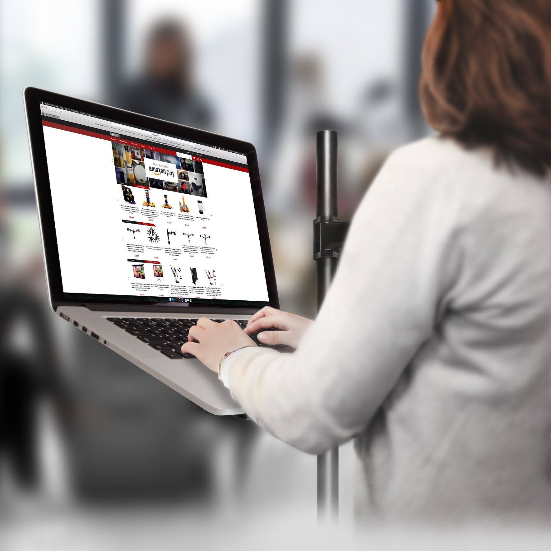 Duronic Monitor and Laptop Stand with a person using a laptop mounted on a pole stand while browsing an e-commerce website.
