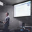 Duronic Projector Screen Electric with a man standing at a podium