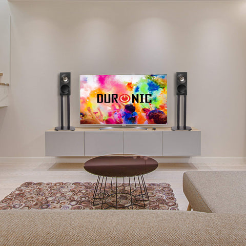 Duronic SPS1022-40 Speaker Stand featuring a flat-screen TV on a floating white console, flanked by two black bookshelf speakers on tall Duronic floor stands.