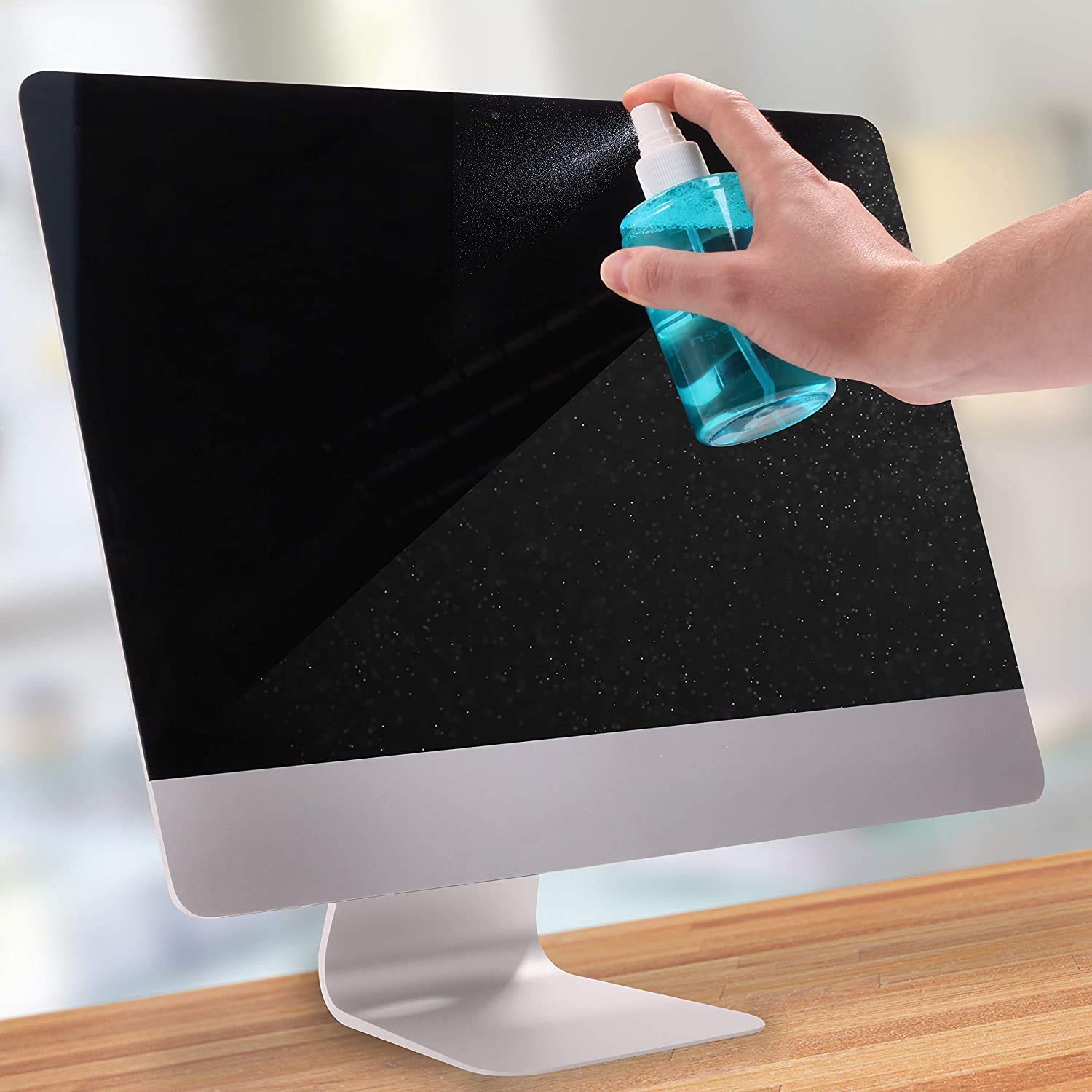 Duronic Screen Cleaner with a Hand spraying blue cleaning liquid onto a dusty desktop computer screen on a wooden table.