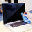 Duronic Screen Cleaner with a Hand wiping a dirty laptop screen with a blue microfiber cloth on a desk.