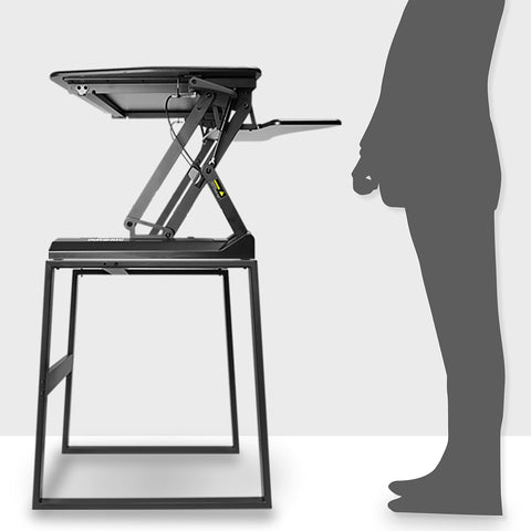 Duronic Sit-Stand Desk Frame on a black frame table next to a person's silhouette.