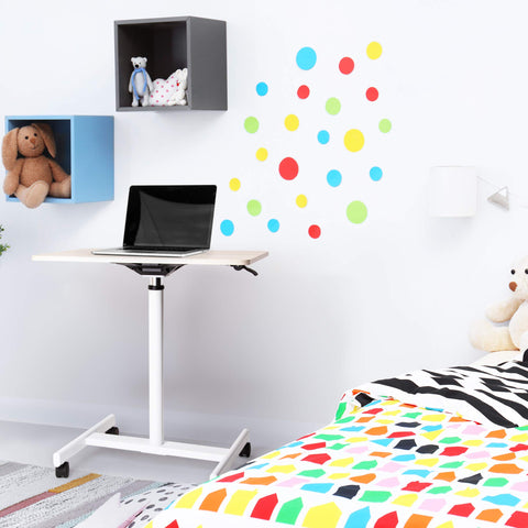 Duronic Sit-Stand Desk WPS67 with a laptop sits in a brightly colored children's bedroom featuring polka dot wall decals and stuffed animals.
