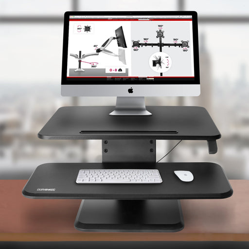 Duronic Sit-Stand Desk featuring a two-tier design with an iMac on the top shelf and a wireless keyboard and mouse on the lower tray.