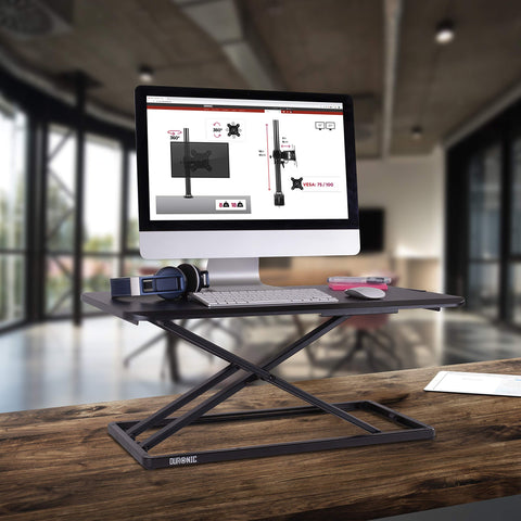 Duronic Sit-Stand Desk on a wooden table holding a computer and headphones.