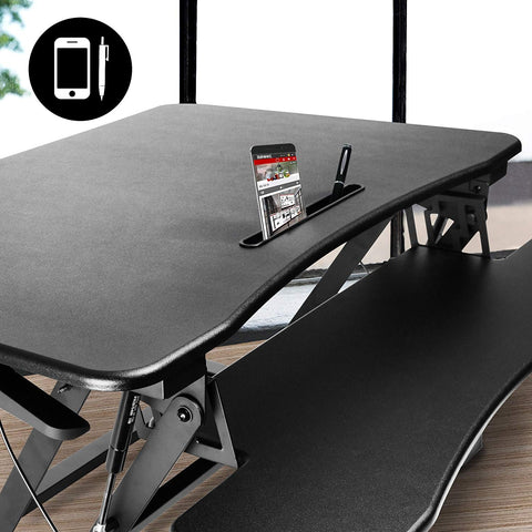 Duronic Sit-Stand Desk with built-in slot holding a smartphone and pen.
