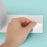 Duronic Thermal Labels with hand peeling the corner of a white sticker sheet from a teal background.