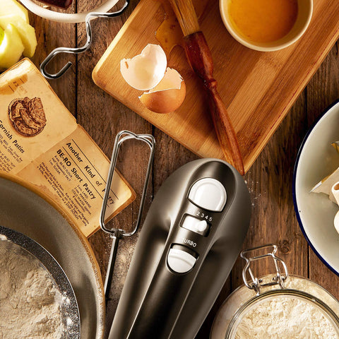 Top-down view of a dark grey electric hand mixer on a rustic baking table.